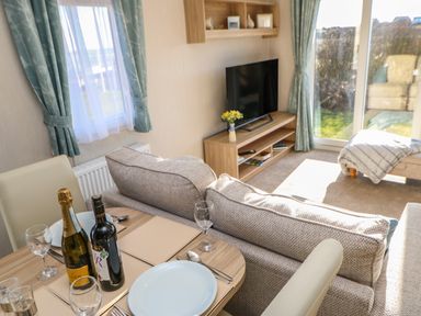 A dining area with a table set with plates wine glasses and bottles next to a sofa facing a TV in a living room at Wansbeck View 2 in Ashington