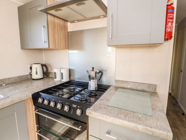 A kitchen with a gas stove kettle coffee maker and storage cabinets at Wansbeck View 2 in Ashington