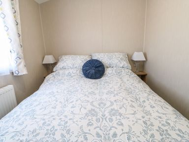 A bedroom with a bed covered in floral bedding and two bedside tables with lamps at Wansbeck View 2 in Ashington