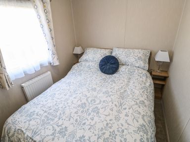 A bedroom with a bed with floral bedding a blue round pillow and bedside tables with lamps at Wansbeck View 2 in Ashington
