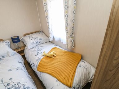 A small bedroom with two single beds a nightstand with a blue lamp yellow blanket and a stuffed toy on one bed at Wansbeck View 2 in Ashington