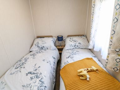 A bedroom with two single beds with floral bedding a yellow blanket and a giraffe toy at Wansbeck View 2 in Ashington