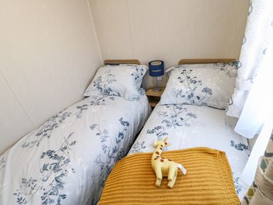 A bedroom with two single beds floral bedding a yellow blanket and a giraffe toy at Wansbeck View 2 in Ashington