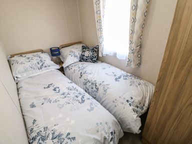 A bedroom with two single beds with floral bedding a bedside table with a blue lamp and a window with patterned curtains at Wansbeck View 2 in Ashington