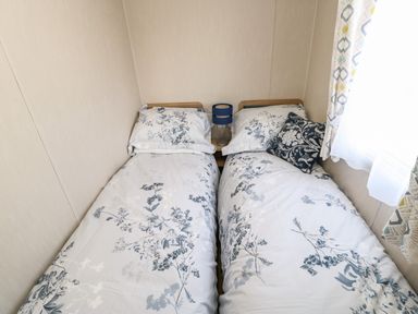 A bedroom with two single beds with floral bedding a bedside table and lamp between them at Wansbeck View 2 in Ashington