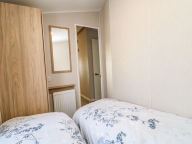 A bedroom with two single beds a wooden wardrobe a wall mirror and an open door at Wansbeck View 2 in Ashington