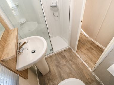 A bathroom with a sink pedestal shower with glass door and wooden floor at Wansbeck View 2 in Ashington