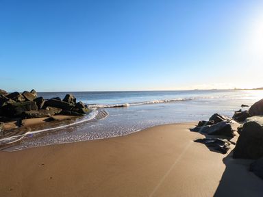 A sandy beach with rocks along the shore and waves meeting the sand at Wansbeck View 2 in Ashington