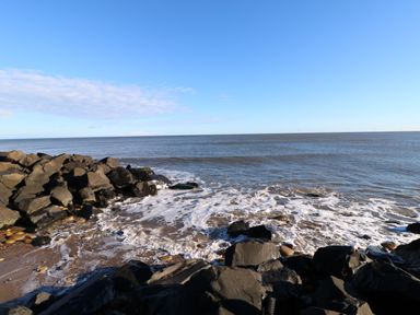 A rocky shoreline with waves washing onto the beach and a blue sky at Wansbeck View 2 in Ashington
