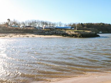A shoreline with boats on land behind a stone barrier and trees in the background at Wansbeck View 2 in Ashington