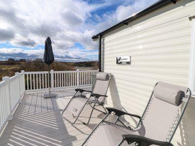 Two reclining chairs and a closed umbrella on a deck next to a mobile home at Wansbeck View 2 in Ashington