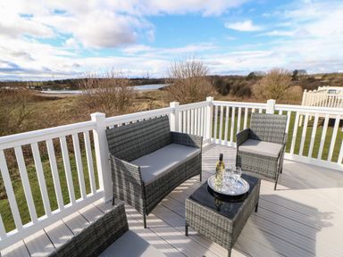 An outdoor patio with wicker furniture and a tray with a bottle and glasses on a table at Wansbeck View 2 in Ashington