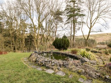 A garden with a stone-bordered pond and trees in the background at The Chapel in Dol-y-Gaer near Pontsticill