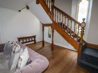 A sitting area with a sofa and cushions near wooden stairs with stained glass windows at The Chapel in Dol-y-Gaer near Pontsticill
