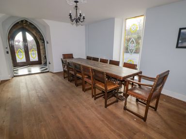 A dining room with long wooden table and chairs near stained glass windows at The Chapel in Dol-y-Gaer near Pontsticill