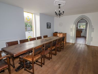 A dining room with a long wooden table and chairs and stained glass window at The Chapel in Dol-y-Gaer near Pontsticill