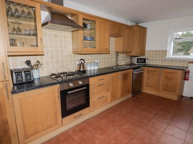 A kitchen with wooden cabinets black countertops a gas stove an oven a toaster and a microwave at The Chapel in Dol-y-Gaer near Pontsticill