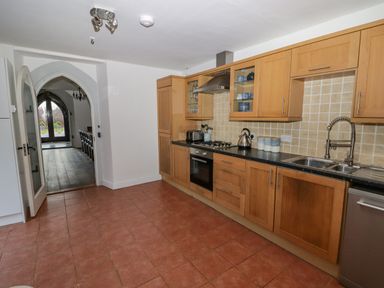 A kitchen with wooden cabinets and black countertops with a double sink and gas stove at The Chapel in Dol-y-Gaer near Pontsticill