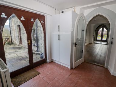 A hallway with arched glass door opening to a room with wooden floor and stained glass windows at The Chapel in Dol-y-Gaer near Pontsticill