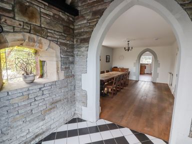 A dining room with wooden table and chairs seen through an arched doorway with stone walls and a tile floor at The Chapel in Dol-y-Gaer near Pontsticill