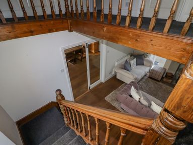 A view down a wooden staircase into a living room with sofas and a rug at The Chapel in Dol-y-Gaer near Pontsticill
