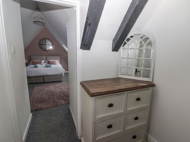 A hallway with a chest of drawers and a mirror leading to a bedroom with a bed and a rug at The Chapel in Dol-y-Gaer near Pontsticill