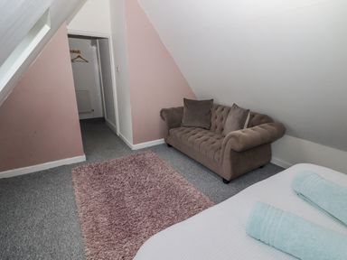 A room with a brown sofa two blue towels on a white bed and a pink rug at The Chapel in Dol-y-Gaer near Pontsticill