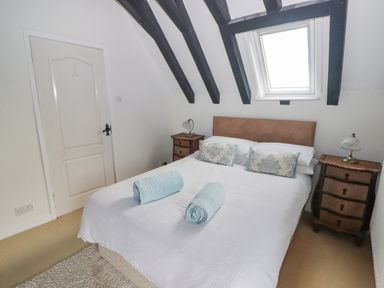 A bedroom with a bed with white bedding and blue pillows and towels a bedside table with a lamp and exposed black ceiling beams at The Chapel in Dol-y-Gaer near Pontsticill