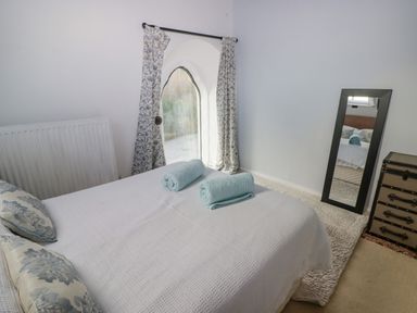 A bedroom with a bed with rolled towels two floral pillows a decorative window curtains a freestanding mirror and a chest of drawers at The Chapel in Dol-y-Gaer near Pontsticill