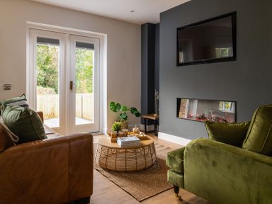 A living room with a brown leather sofa green armchair wooden round coffee table and a wall-mounted television at Sygun in Beddgelert