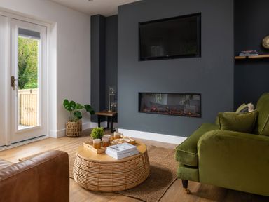 A living room with a green sofa a round wicker coffee table and a built in fireplace at Sygun in Beddgelert