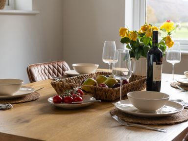A dining table set with bowls plates wine glasses a bottle of wine a fruit basket and flowers at Sygun in Beddgelert