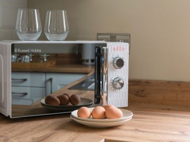 A microwave with two glasses on top and four eggs on a plate on a wooden kitchen counter at Sygun in Beddgelert