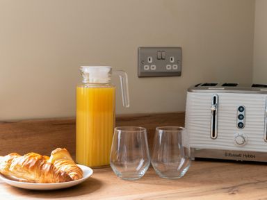 A kitchen counter with a plate of croissants a jug of orange juice two glasses and a toaster at Sygun in Beddgelert