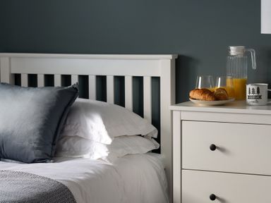 A bed with white bedding and a dark pillow next to a white nightstand with croissants orange juice and a mug on top at Sygun in Beddgelert