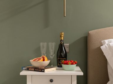 A white bedside table with two books a bowl of sliced grapefruit two empty champagne glasses a bottle of alcohol free sparkling wine and a bowl of strawberries next to a bed at Sygun in Beddgelert