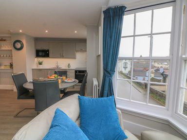 A kitchen and dining area with a round table set for breakfast and a window with blue curtains at Queens View in Dartmouth