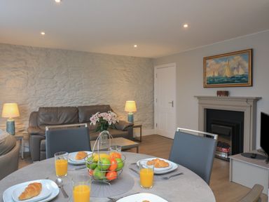 A dining table with plates of croissants and glasses of orange juice in a living room with a brown sofa, lamps, a fireplace, and a painting at Queens View in Dartmouth