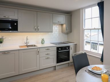 A kitchen with grey cabinets, built-in microwave, oven, stovetop, sink, and a small dining table with a croissant and orange juice at Queens View in Dartmouth