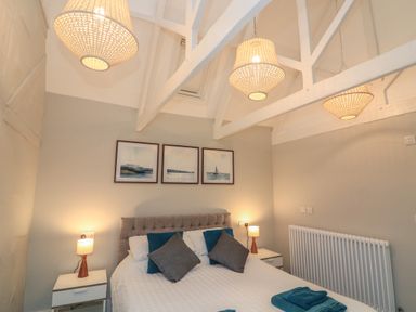 A bedroom with a bed pillows nightstands lamps framed paintings and ceiling lights at Queens View in Dartmouth
