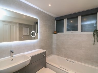 A bathroom with a sink and faucet next to a bathtub below windows with plants at Queens View in Dartmouth
