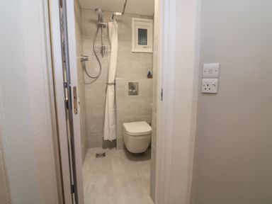 A small bathroom with a wall-mounted toilet and a shower area with a shower curtain at Queens View in Dartmouth