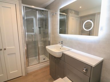 A bathroom with a glass shower enclosure white sink gray cabinets and a large illuminated mirror at Queens View in Dartmouth