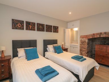 A bedroom with two single beds wooden nightstands and a wooden dresser by a brick fireplace at Queens View in Dartmouth