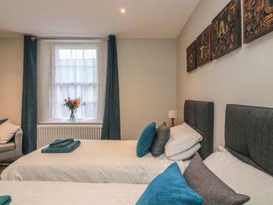 A bedroom with two beds and blue pillows a window with curtains and a vase of flowers Queens View Dartmouth
