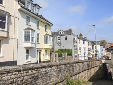 A street with multi story houses and parked cars along a stone wall at Queens View in Dartmouth
