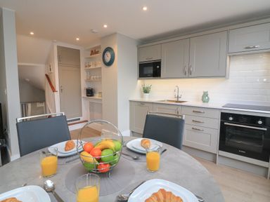A kitchen with gray cabinets, a round dining table set with croissants and orange juice, and a basket of fruit at Queens View in Dartmouth