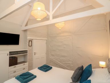 A bedroom with a bed towels a chest of drawers a wall-mounted tv and pendant lights at Queens View in Dartmouth