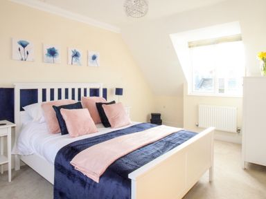 A bedroom with a white bed frame navy and pink bedding bedside tables and a window at Anchors Away in Weymouth