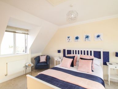 A bedroom with a bed and pillows two nightstands a chair and a side table near a window at Anchors Away in Weymouth